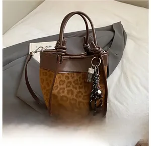 Détail du sac seau léopard avec bordure marron et breloques tressées sur un drap blanc