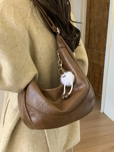 Brown leather hobo shoulder bag with fuzzy charm and adjustable strap worn on wool coat