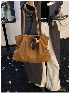 Detail of caramel leather tote bag featuring a crochet bear charm and rich pebbled texture