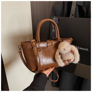 Detail of dark brown glossy leather handbag with vintage buckle and plush rabbit charm