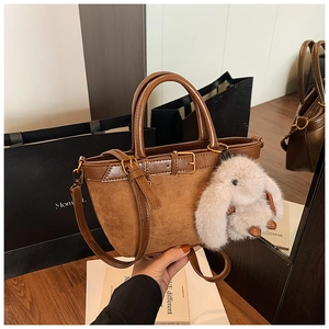 Close-up of brown bucket bag showing mixed leather textures and white rabbit pendant