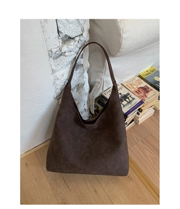 Close-up of a large dark brown suede tote bag leaning against a rustic brick wall