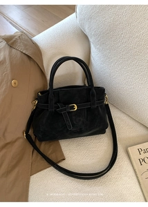 Detail of black suede tote bag featuring gold buckle accents and long shoulder strap