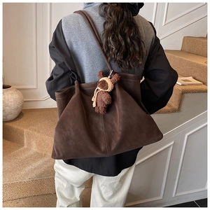 Detail of dark brown matte tote bag with teddy bear charm on model in minimalist interior