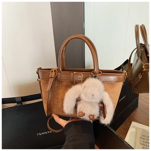 Detail of a brown leather and suede handbag with a plush bunny and strap on a display