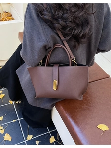 Detail view of deep brown pebbled leather bucket bag with a vertical gold metal buckle