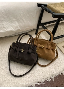 Detail of retro suede tote bags in brown and tan with decorative buckle on white faux fur