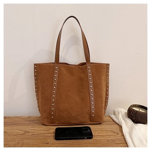Detailed close-up of brown suede tote bag with silver studs on a wooden table surface