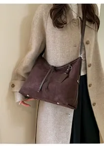 Détail d'un sac cabas en daim marron foncé avec pompons sur un manteau beige