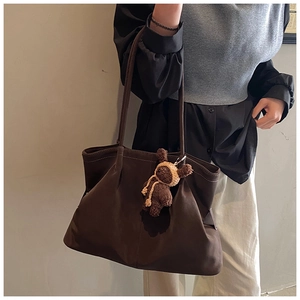 Detail of dark brown matte tote bag featuring a cute teddy bear charm on shoulder strap