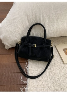 Detail of black faux suede tote bag featuring golden buckle and soft pleated texture