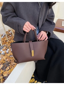 Detail of dark brown pebble leather tote bag with gold hardware in outdoor autumn setting