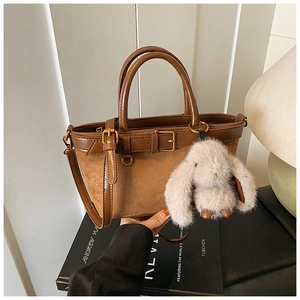 Detail view of brown suede bucket bag with a plush bunny charm and leather strap