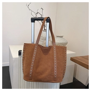 Detail view of large brown suede tote bag with silver studs on a white suitcase
