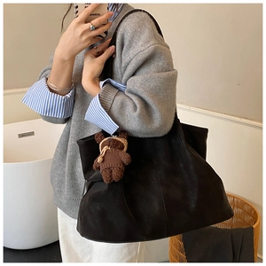 Detail of a large black matte tote bag featuring a cute brown plush bear charm accessory