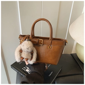 Detailed view of a vintage brown leather handbag featuring a plush rabbit pendant and buckle