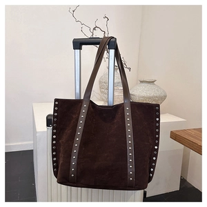 Detail of dark brown suede tote bag with silver studs hanging on a white suitcase