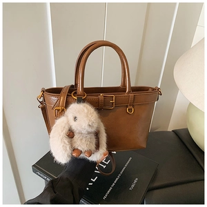 Detail of a brown leather tote bag with a gold buckle and cute plush bunny charm