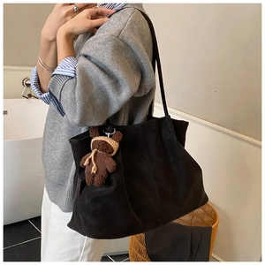 Detail of black frosted leather tote bag with a cute brown knitted bear charm accessory