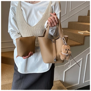 Bolso cubo de grano lichi con colgante de oso de peluche mostrado en un entorno de escalera