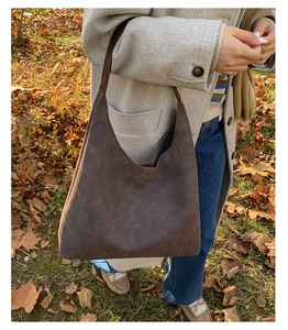 Detail of a large brown suede tote bag carried by a model in an autumn outdoor setting