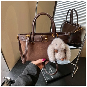 Detail of dark brown suede bucket bag with gold buckle and grey bunny charm