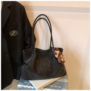 Detail of black matte tote bag with bear charm on a silver suitcase for travel
