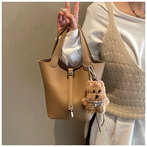 Detalle del bolso de cubo camel con patrón de lichi, cierre plateado y colgante de peluche