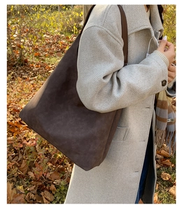 Close-up of deep brown suede tote bag featuring a wide shoulder strap in autumn setting