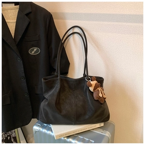 Detail of black suede tote bag with brown bear charm on a silver suitcase