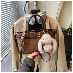 Detail of dark brown tote bag with suede texture, buckle accents and plush rabbit charm