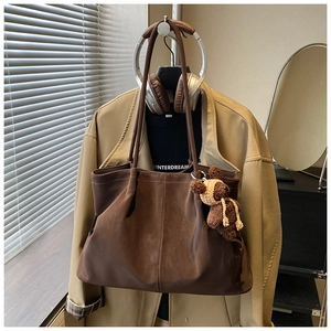 Detail of dark brown matte tote bag featuring a cute knitted bear charm on the handle