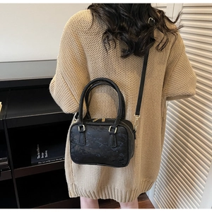 Detail of black marble textured crossbody bag with gold hardware on beige knit sweater
