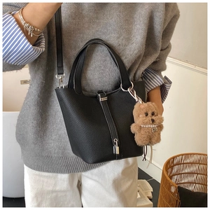 Detalle de bolso cubo negro de piel con cierre metálico y adorno de oso de peluche
