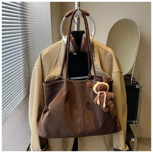 Detail of dark brown matte suede tote bag featuring a cute plush bear charm on strap