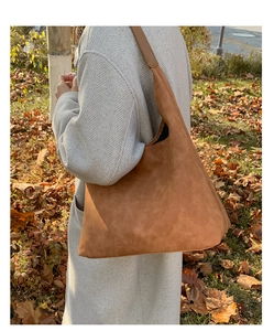Outdoor shot of a caramel suede hobo bag styled for autumn with fallen leaves