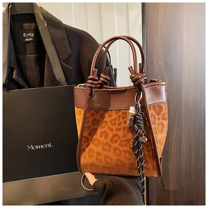 Détail d'un sac seau léopard avec poignées en cuir marron et pendentifs décoratifs