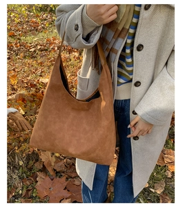 Close-up of a brown suede tote bag carried by a model in a stylish autumn outdoor setting