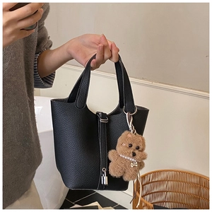 Detalle de bolso tipo cubo negro de piel granulada con cierre plateado y oso de peluche
