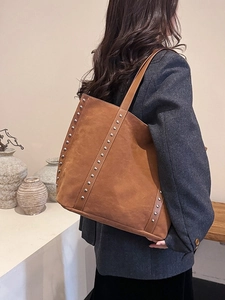 Brown suede tote bag with silver studs worn by a model in a grey blazer for office style