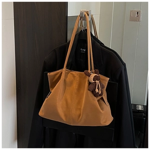 Close-up of a brown tote bag with a cute bear charm hanging on a black suit jacket