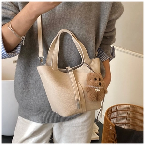 Detalle del bolso de cubo blanco crema con patrón de lichi y pequeño candado con oso