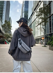 Outdoor street view of a grey plaid crossbody chest bag worn on back with adjustable strap