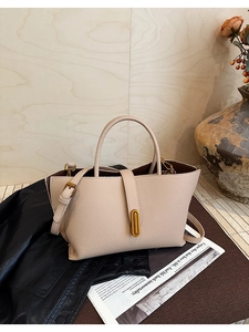 Detail of beige lychee grain leather handbag featuring a gold oval clasp and crossbody strap