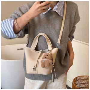 Detalle de bolso cubo beige con textura lichi, cierre de metal y colgante de oso