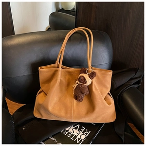 Detailed shot of caramel matte tote bag with knit bear charm on a dark leather sofa