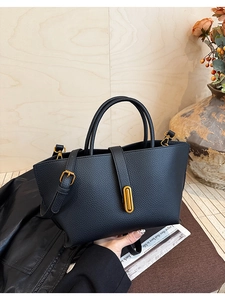 Detail of black pebbled leather tote featuring elegant gold oval lock and dual handles