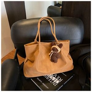 Detail of a camel large tote bag on a black leather seat with a crochet bear charm