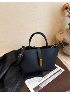 Detail of vintage black litchi grain leather tote with golden buckle and textured finish