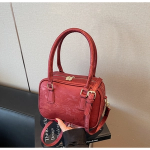 Close-up of burgundy suede Boston bag featuring gold hardware and wrinkled texture